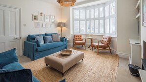 Una sala de estar con un sofá azul, un otoman beige y dos sillones de cuero.