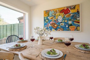 A dining table set with plates, glasses, and a vase of flowers, with a colorful painting above. - 21 Park Lane, Aldeburgh (Suffolk)
