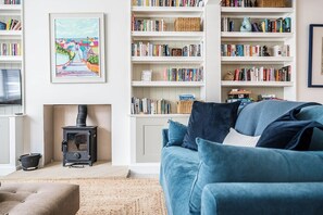A cozy living room with a sofa, a bookshelf, a fireplace, and a painting on the wall. - 21 Park Lane, Aldeburgh (Suffolk)