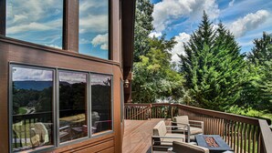 Una terraza de madera con mobiliario exterior y un ventanal grande que da a una zona boscosa.