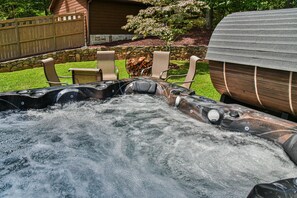 A hot tub surrounded by chairs, with a stone wall and wooden fence in the background. - Bent Creek Chalet, Sauna,Jacuzzi,Fire pit and OD shower (Asheville)