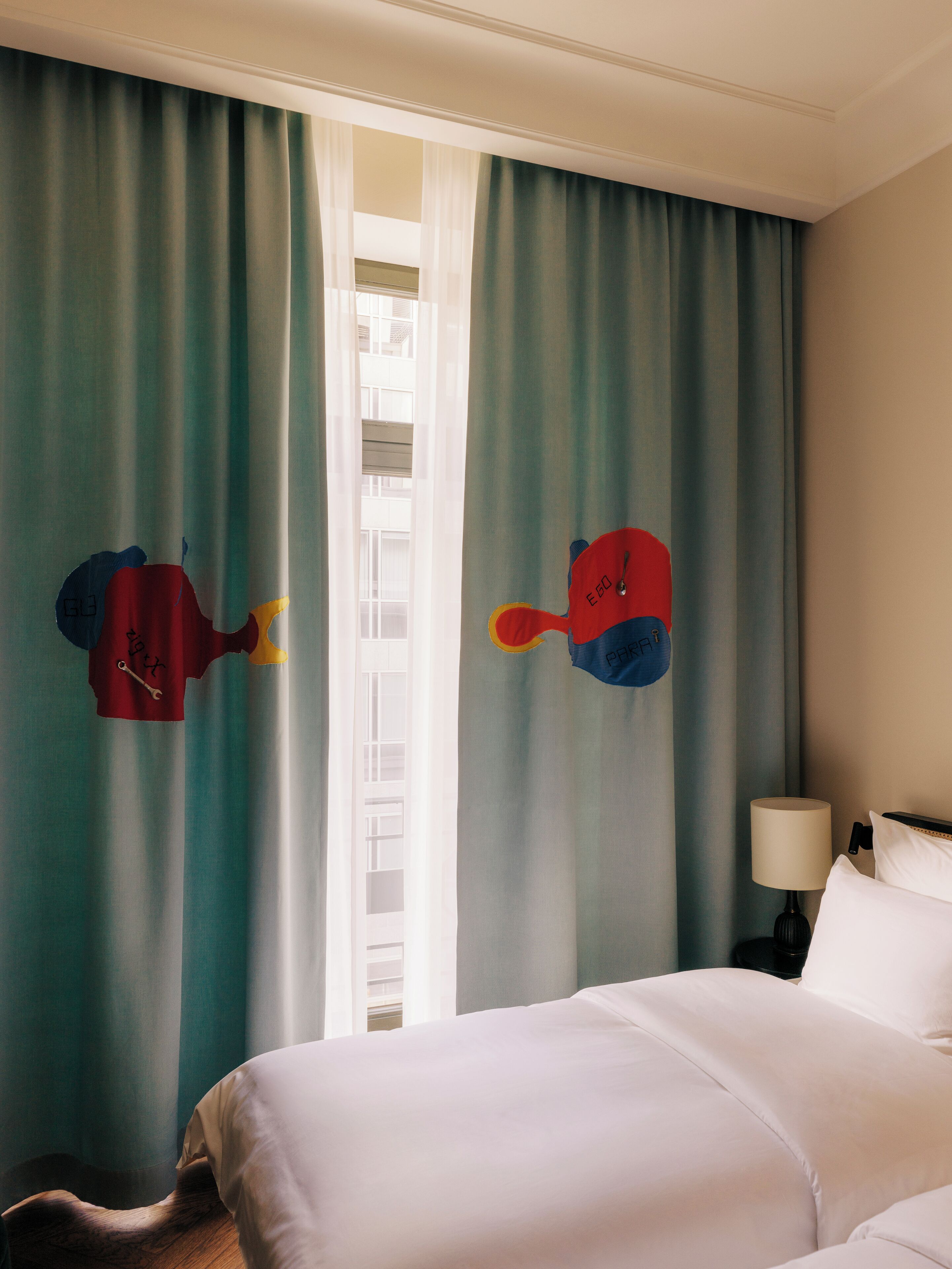 Habitación de hotel con cama, mesita de noche con lámpara y cortinas de diseño colorido.