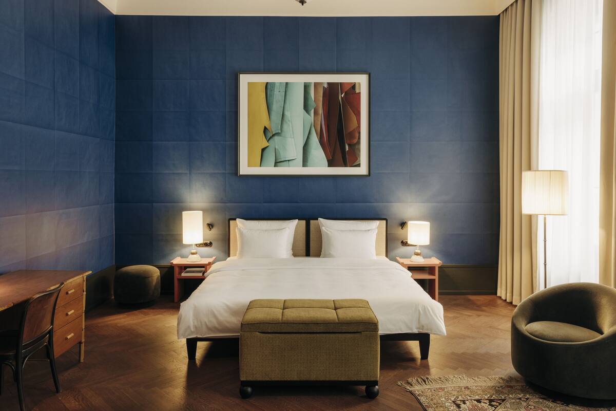 Une chambre d’hôtel avec un grand lit, deux tables de chevet avec des lampes, un bureau, une chaise et un grand tableau abstrait accroché au mur.