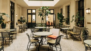 A spacious indoor area with multiple tables and chairs, a high ceiling with a skylight, and various potted plants. - Château Royal Berlin (Berlin)