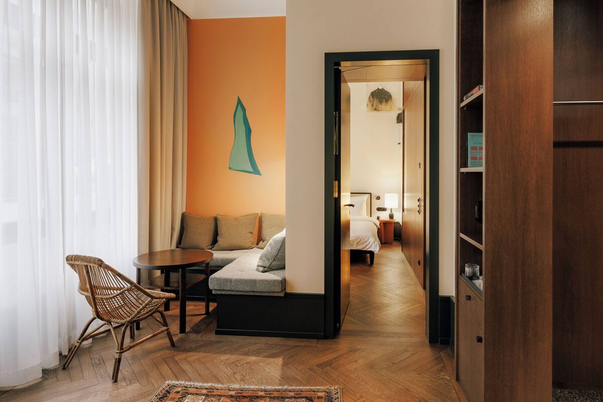 Une chambre d’hôtel avec un plancher en bois, un canapé, une chaise, une petite table et une armoire.