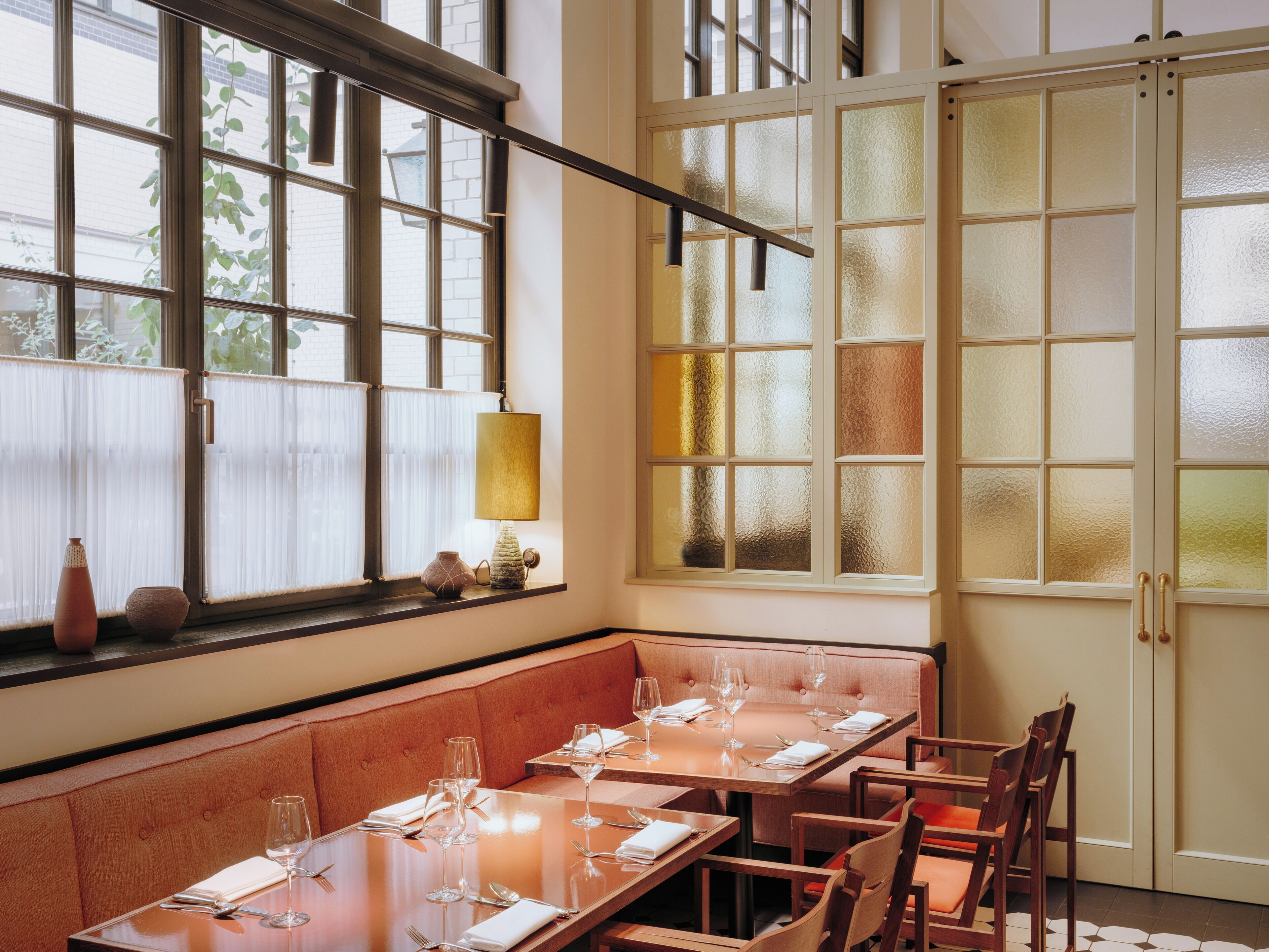 A dining area with a long table set for four, a cushioned bench, and a window with frosted glass panels.