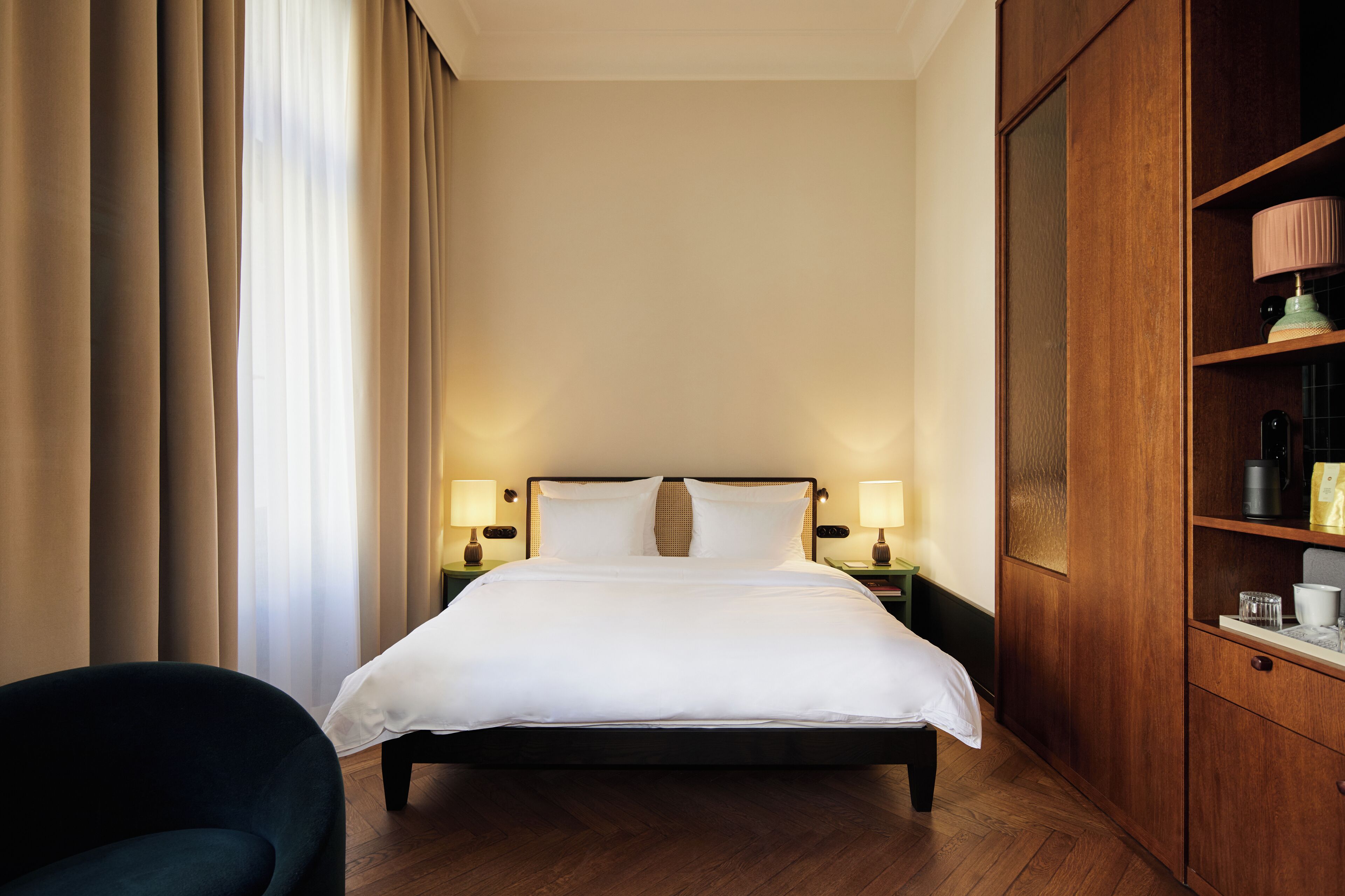 A hotel room with a large bed, two bedside lamps, a wooden wardrobe, and a chair.