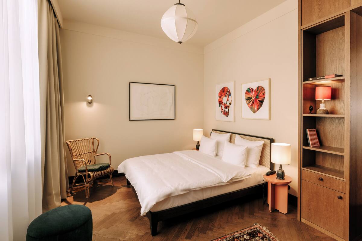 Une chambre à coucher comprenant un lit, une chaise, une table de chevet, une lampe et une bibliothèque.