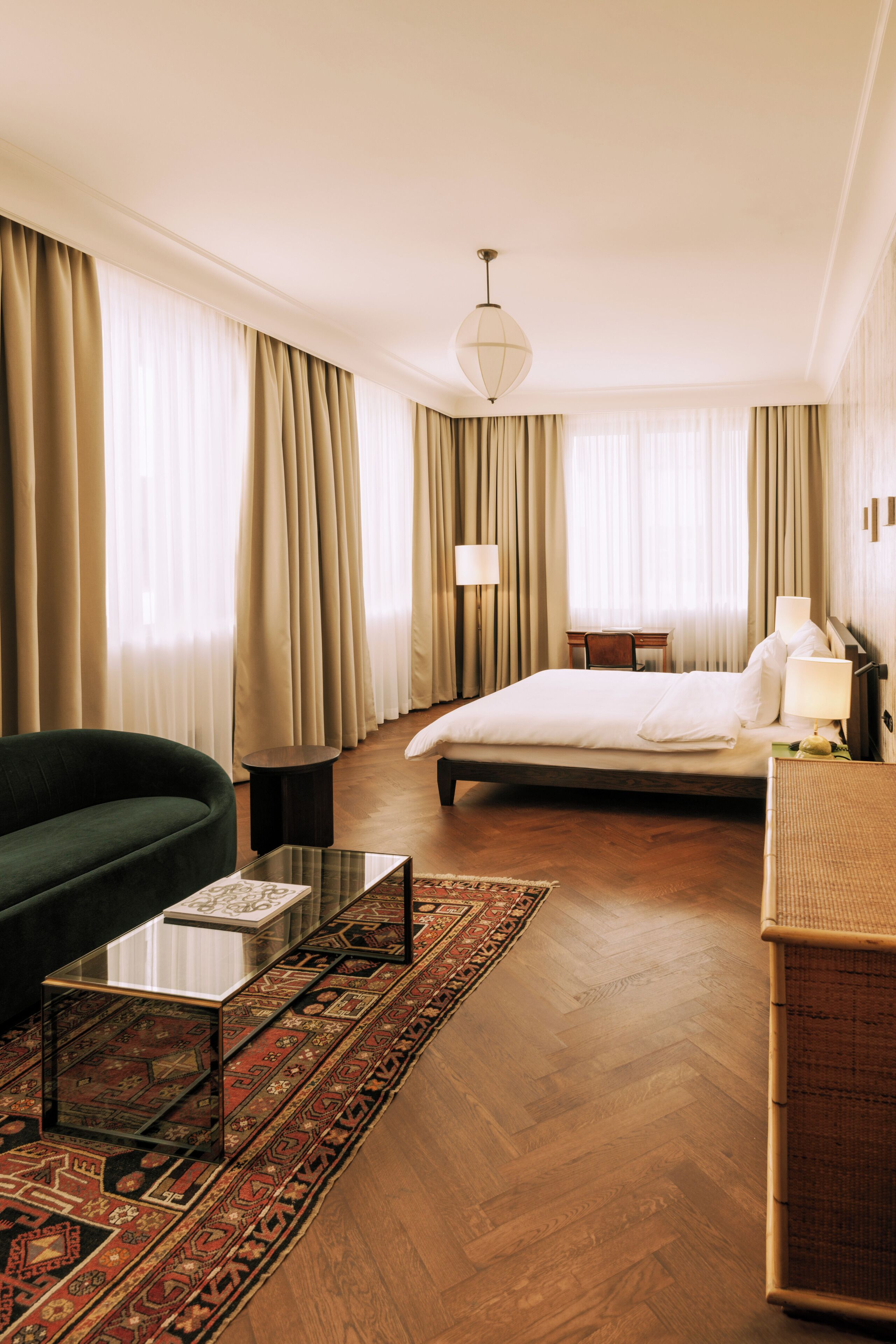 A hotel room with a bed, a green sofa, a glass coffee table, a desk, and a lamp.