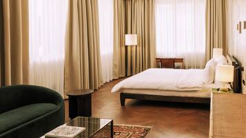 A hotel room with a bed, a green sofa, a glass coffee table, a desk, and a lamp.