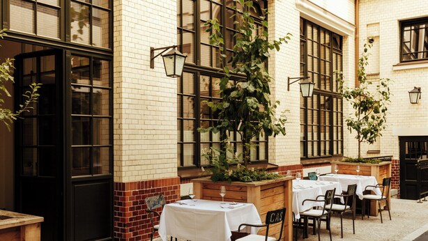 An outdoor cafe with tables and chairs, brick walls, and large windows. - Château Royal Berlin (Berlin)