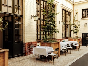 An outdoor cafe with tables and chairs, brick walls, and large windows. - Château Royal Berlin (Berlin)