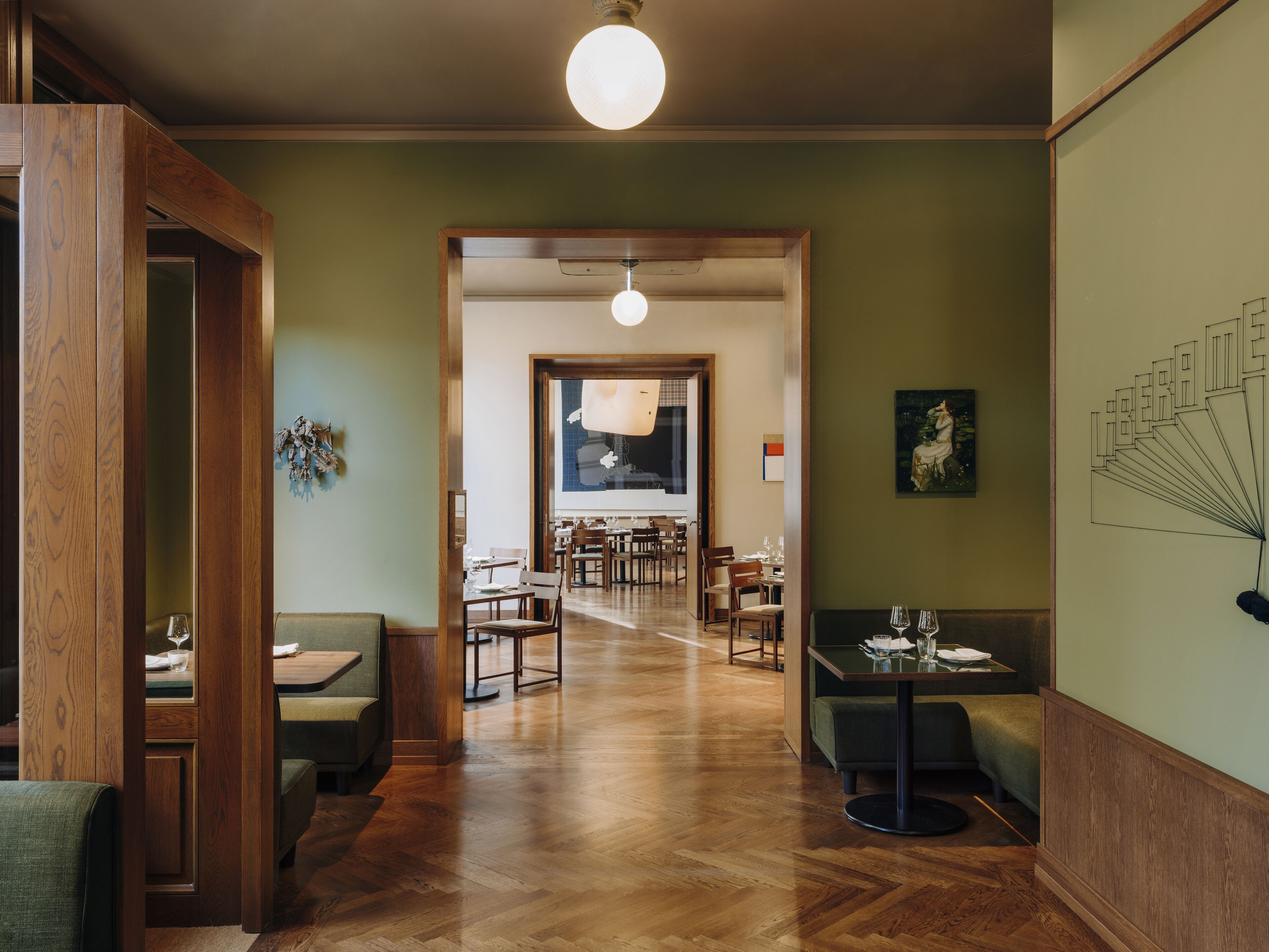 Restaurante com piso de madeira, paredes verdes e uma área de refeições central com mesas e cadeiras.