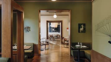 Restaurante com piso de madeira, paredes verdes e uma área de refeições central com mesas e cadeiras.