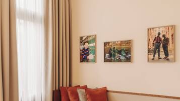 A modern living room with a green armchair, a wooden bench with cushions, and a round wooden table. There are three framed artworks on the wall.
