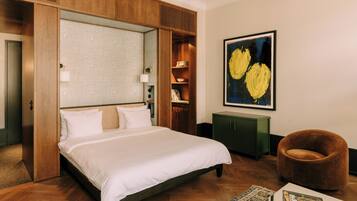 Une chambre d’hôtel avec un grand lit, une armoire en bois, un meuble vert, un fauteuil marron et un tableau au mur.