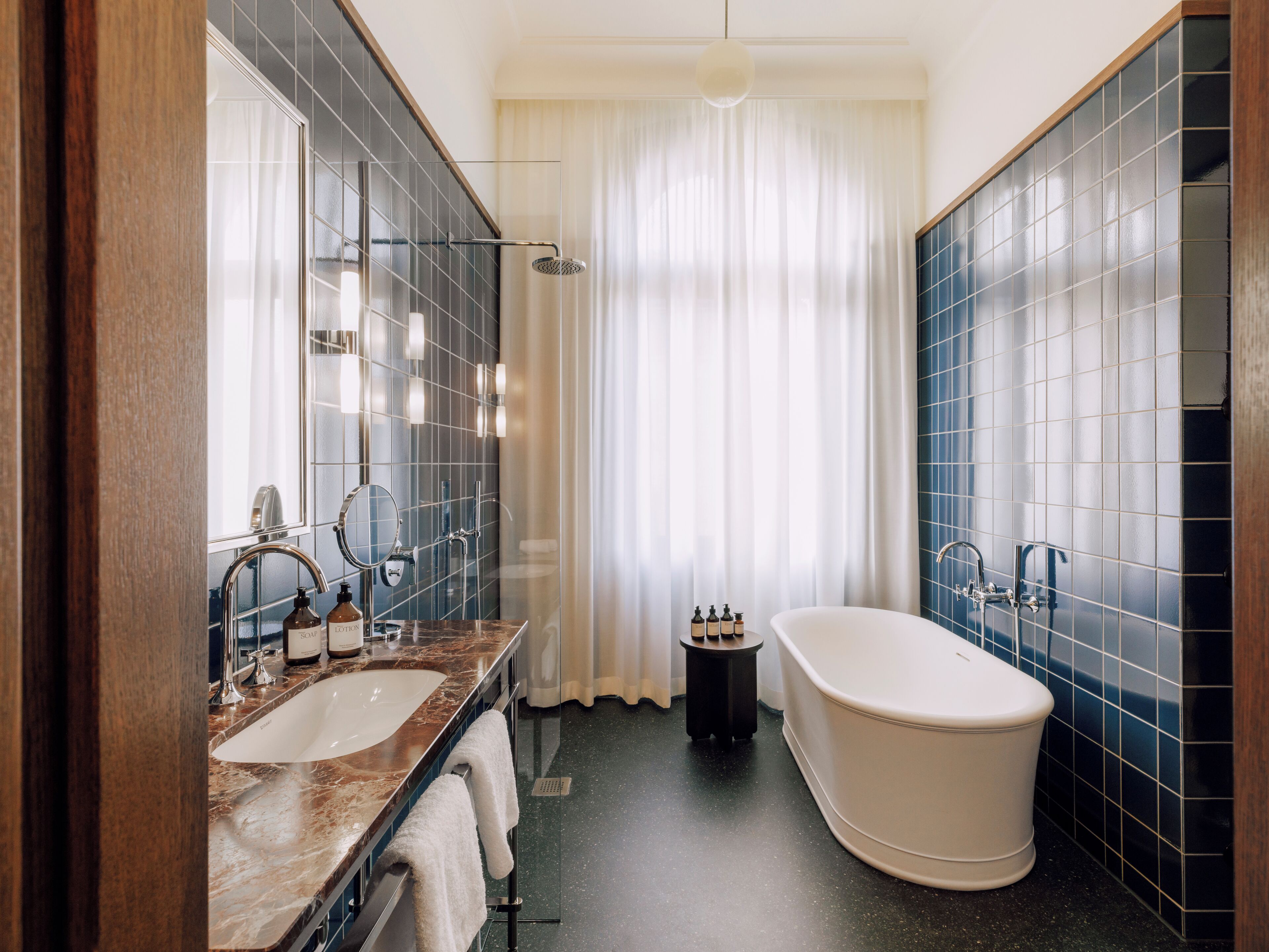 Un baño moderno con una bañera independiente, un espejo grande y un tocador con lavabo y toallero.