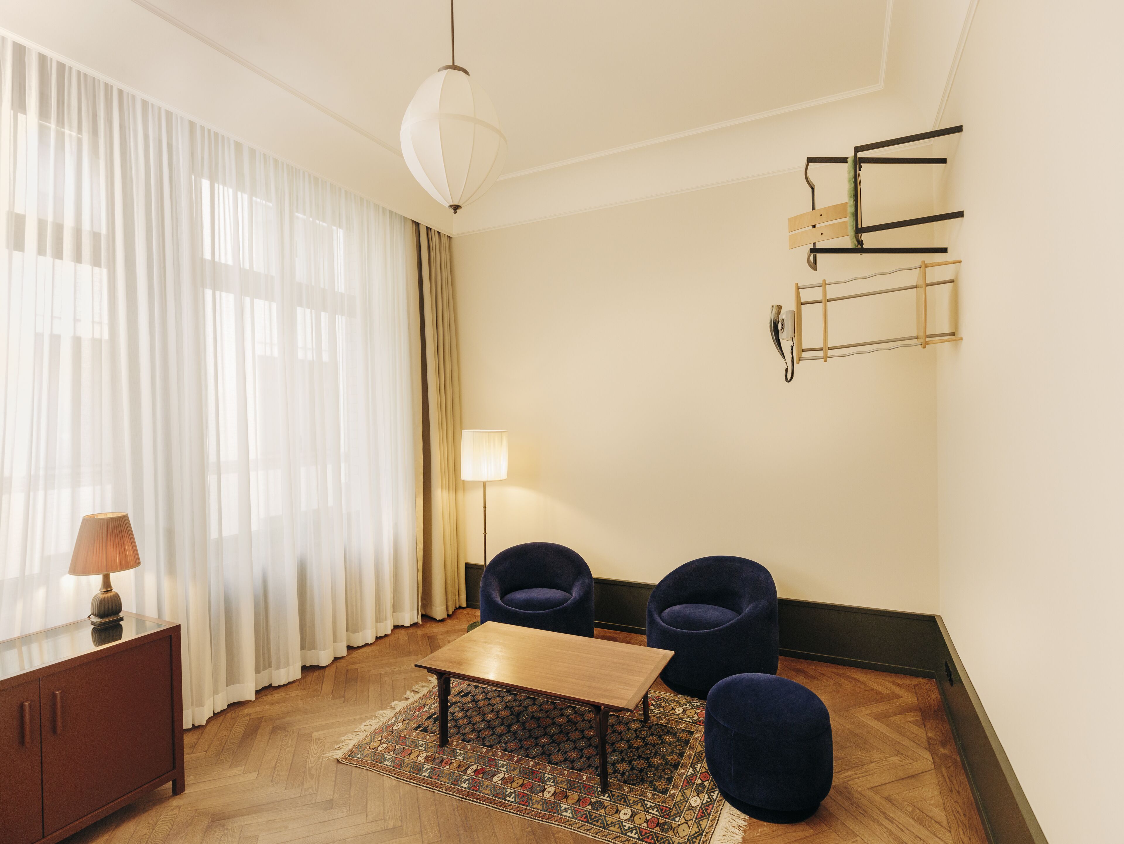 Una habitación moderna con una mesita de centro de madera, dos sillones azules, una lámpara y una alfombra estampada.