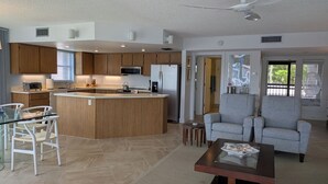 A modern kitchen with wooden cabinets, a central island, and a dining area with a glass table and chairs. - NEW NEW   Burnt Store Marina Front,  Premier Corner Unit, 30-Day Minimum Retreat (Punta Gorda)
