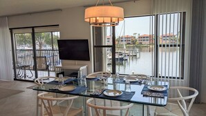 A dining area with a glass table, white chairs, and a view of a marina through large windows. - NEW NEW   Burnt Store Marina Front,  Premier Corner Unit, 30-Day Minimum Retreat (Punta Gorda)