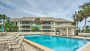 A swimming pool with lounge chairs and a covered area, surrounded by palm trees and a building with multiple balconies. - NEW NEW   Burnt Store Marina Front,  Premier Corner Unit, 30-Day Minimum Retreat (Punta Gorda)