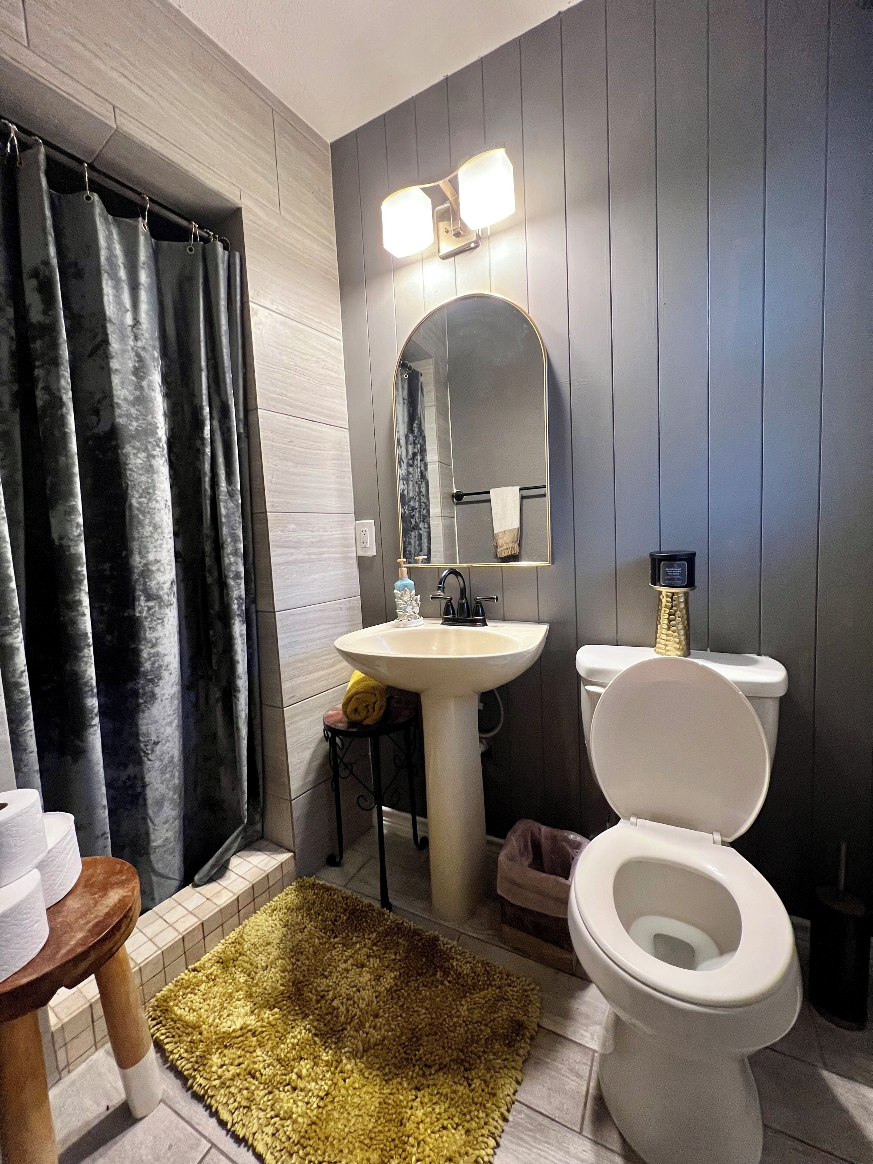 Une salle de bain avec un lavabo blanc, des toilettes, un miroir et un rideau de douche.