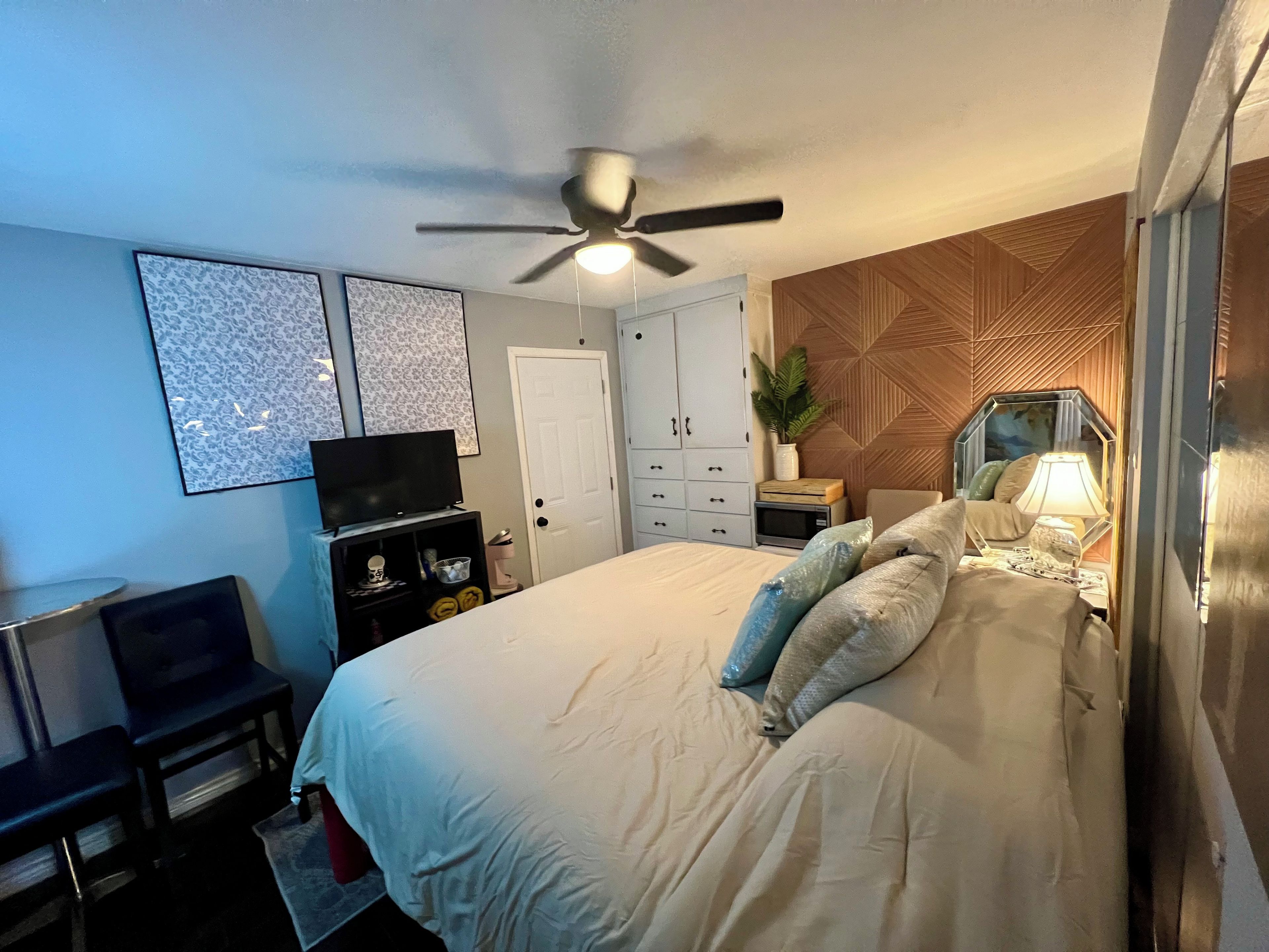 Un dormitorio con cama, ventilador de techo, televisor, escritorio y armario.
