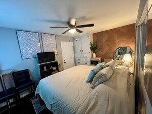 Une chambre à coucher comprenant un lit, un ventilateur de plafond, une télévision, un bureau et une armoire.