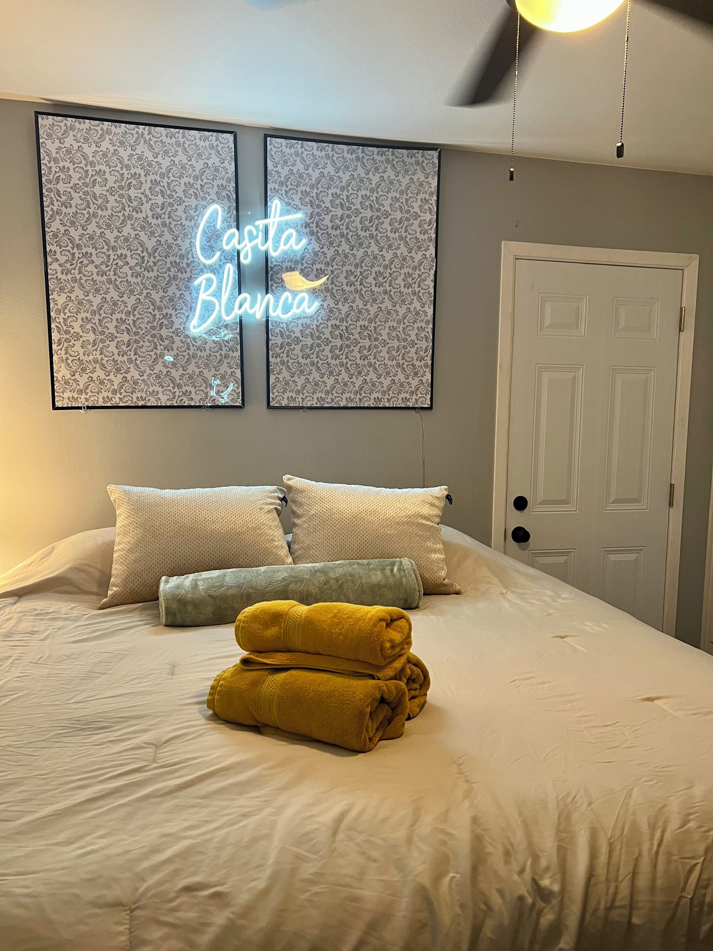 A bedroom with a bed, pillows, a folded towel, and a door.