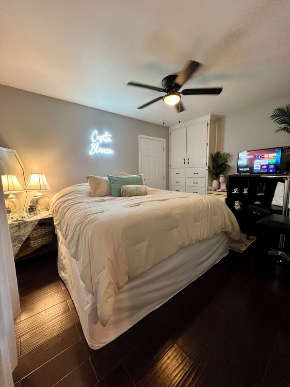 A bedroom with a bed, a ceiling fan, a TV, a wardrobe, and a neon sign.