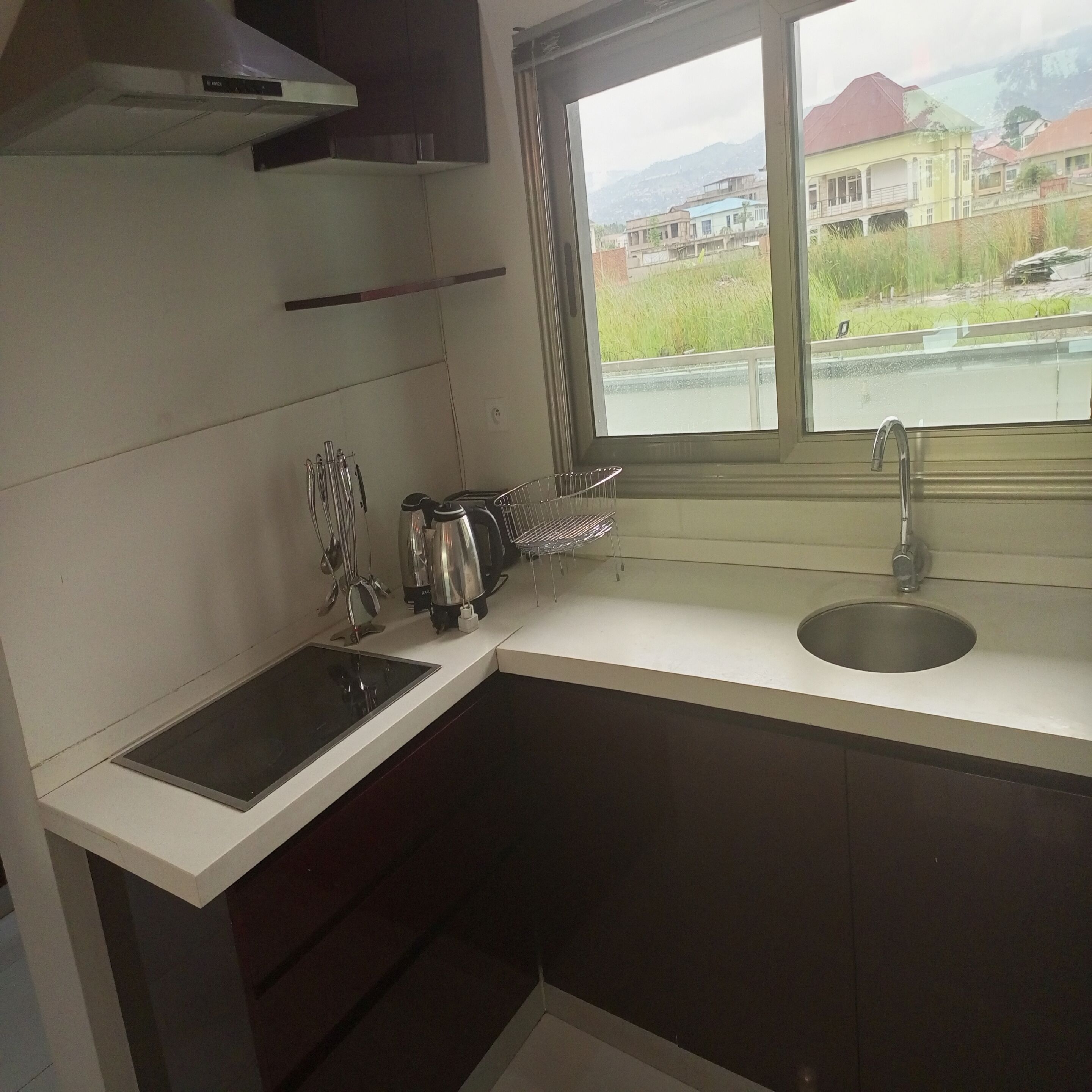 Een kleine keuken met een spoelbak, kookplaat en raam met uitzicht op een straat.