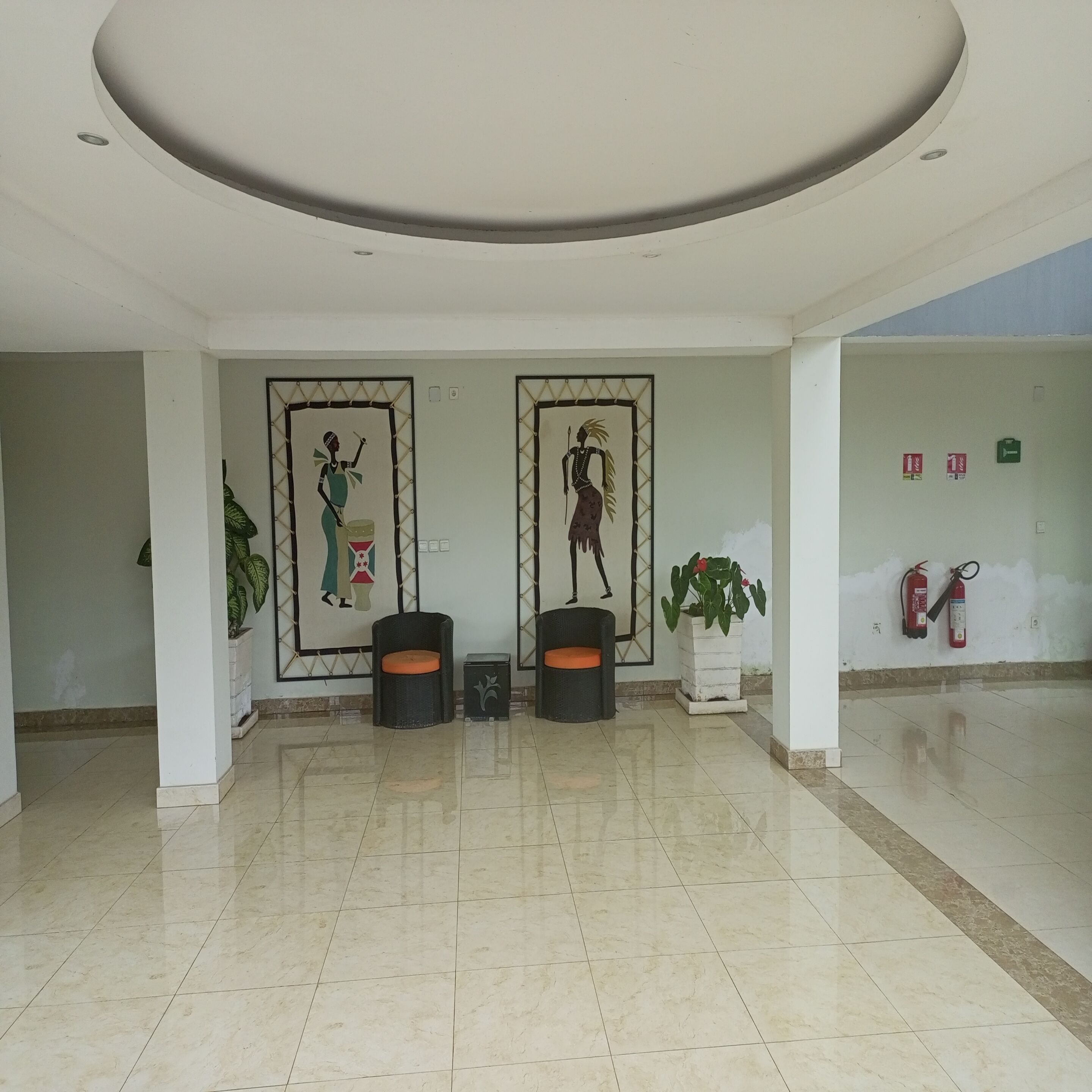 A spacious lobby with a high ceiling, two framed wall art pieces, a potted plant, and a fire extinguisher.