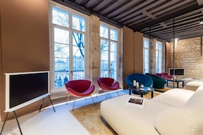 Un salon moderne doté de grandes fenêtres, d’un téléviseur à écran plat et de sièges aux couleurs vives.
