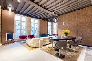 Uma sala de reuniões moderna com uma mesa redonda, várias cadeiras, um sofá e janelas amplas.