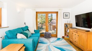 Een woonkamer met een blauwgroene bank, een houten kast, een televisie en een groot raam met uitzicht op het landschap.