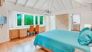 Een slaapkamer met een groot bed, een bureau met stoelen, een televisie en uitzicht op groen buiten de ramen.