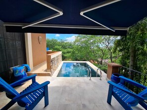 A pool area with a view of greenery, two blue chairs, and a stone wall.