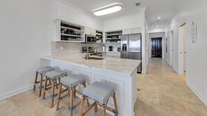 Une cuisine moderne avec des meubles blancs, un grand îlot central doté de tabourets, des appareils en acier inoxydable et un luminaire au plafond qui apporte beaucoup de lumière.