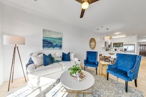A modern living room with a white sofa, blue armchairs, a round coffee table, and a floor lamp.