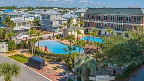 Un quartier résidentiel doté d’une piscine, entourée de maisons, de palmiers et d’un espace de détente extérieur abrité.