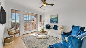 Un salon spacieux doté d’une grande fenêtre, d’un ventilateur de plafond et d’un canapé recouvert d’un tissu bleu.