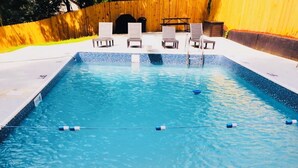Una piscina rectangular con agua cristalina y azul, rodeada por una valla de madera y equipada con tumbonas.