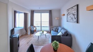 Una habitación de hotel moderna con balcón, sofá, mesa de comedor y televisión.