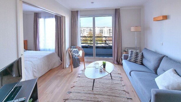 Una habitación de hotel moderna con cama, sofá y balcón con vistas a edificios.