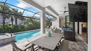 An outdoor pool area with a wooden table and chairs, a ceiling fan, and a view of the pool and surrounding greenery. - 2023 Captiva Home | Steps to The Beach/Shops/Dining (Marco Island)