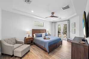 A bedroom with a large bed, a sofa, a wooden cabinet, and a ceiling fan. - 2023 Captiva Home | Steps to The Beach/Shops/Dining (Marco Island)