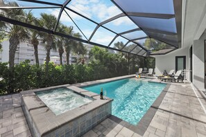 An outdoor infinity pool with a hot tub, surrounded by lounge chairs and a canopy.