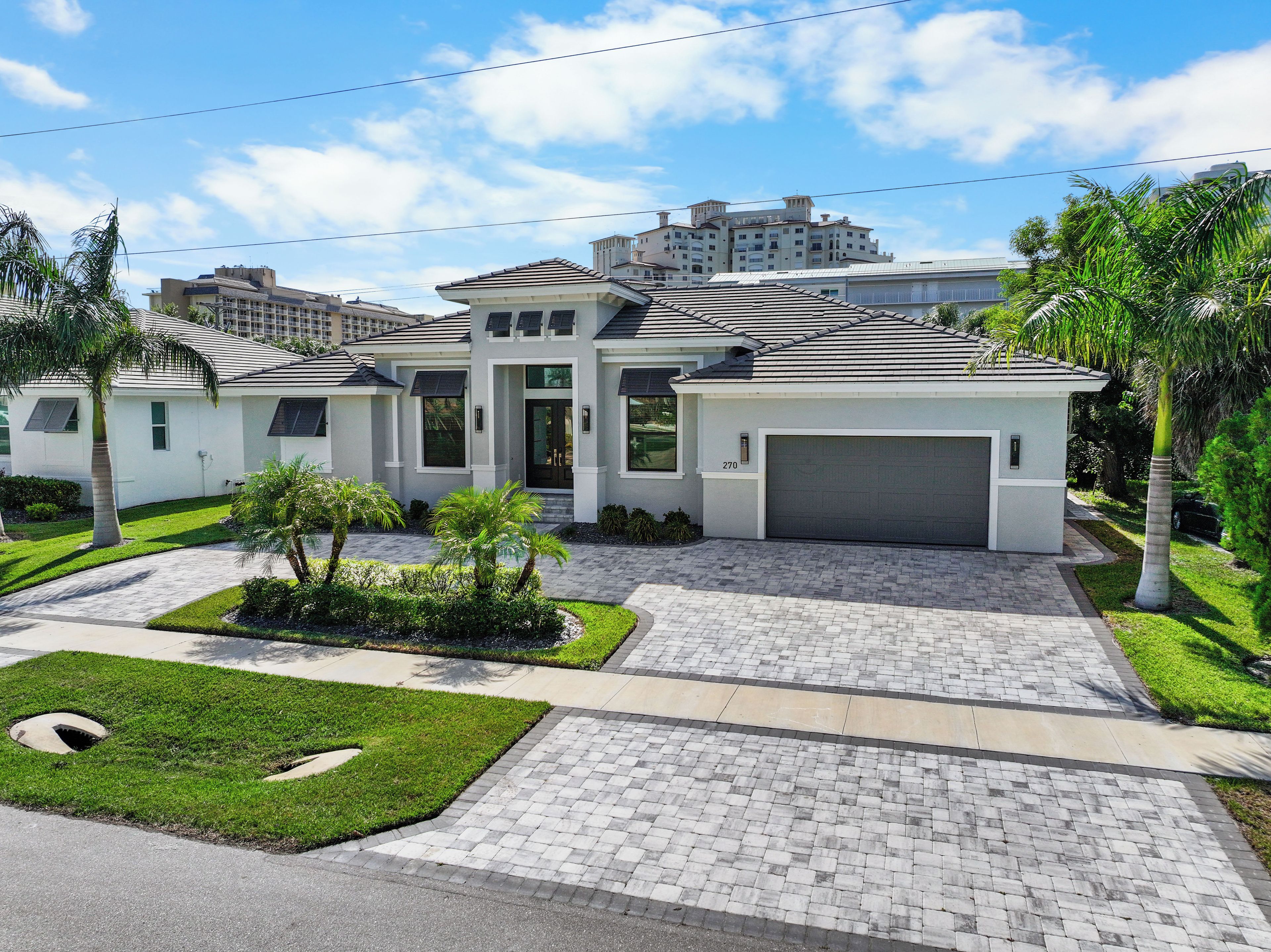 A modern two-story house with a garage, surrounded by well-maintained lawns and palm trees.