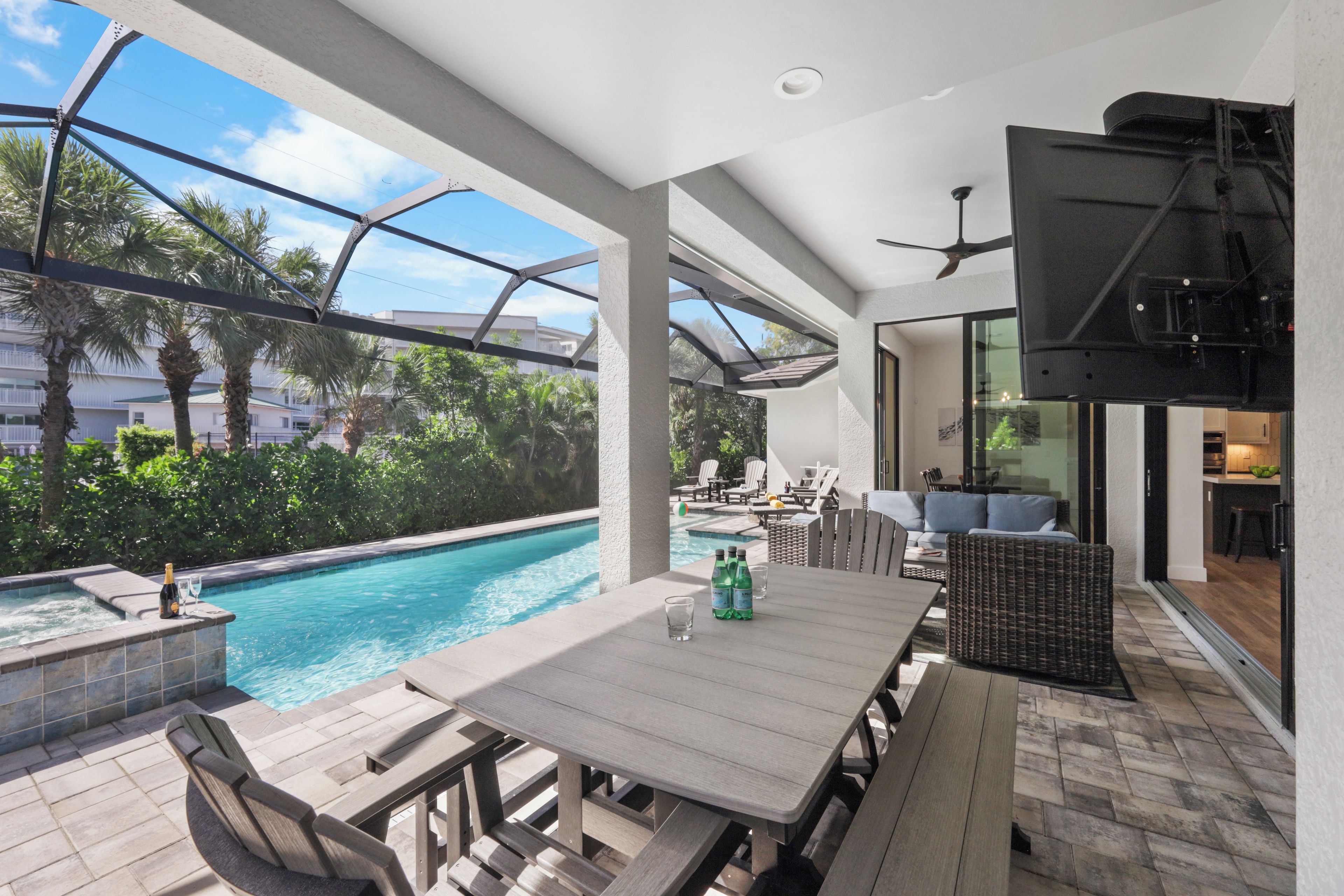 Un espace extérieur avec une piscine, une table et des chaises en bois, un ventilateur de plafond et une vue sur la piscine et la végétation environnante.