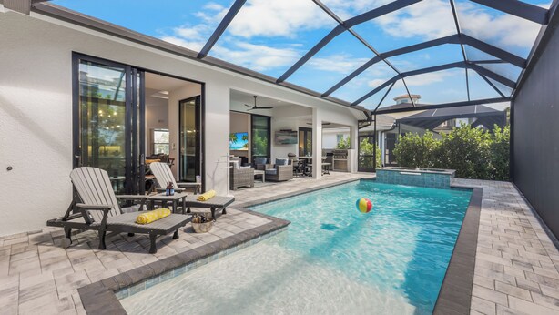 An indoor swimming pool with a glass ceiling, lounge chairs, and a patio area. - 2023 Captiva Home | Steps to The Beach/Shops/Dining (Marco Island)